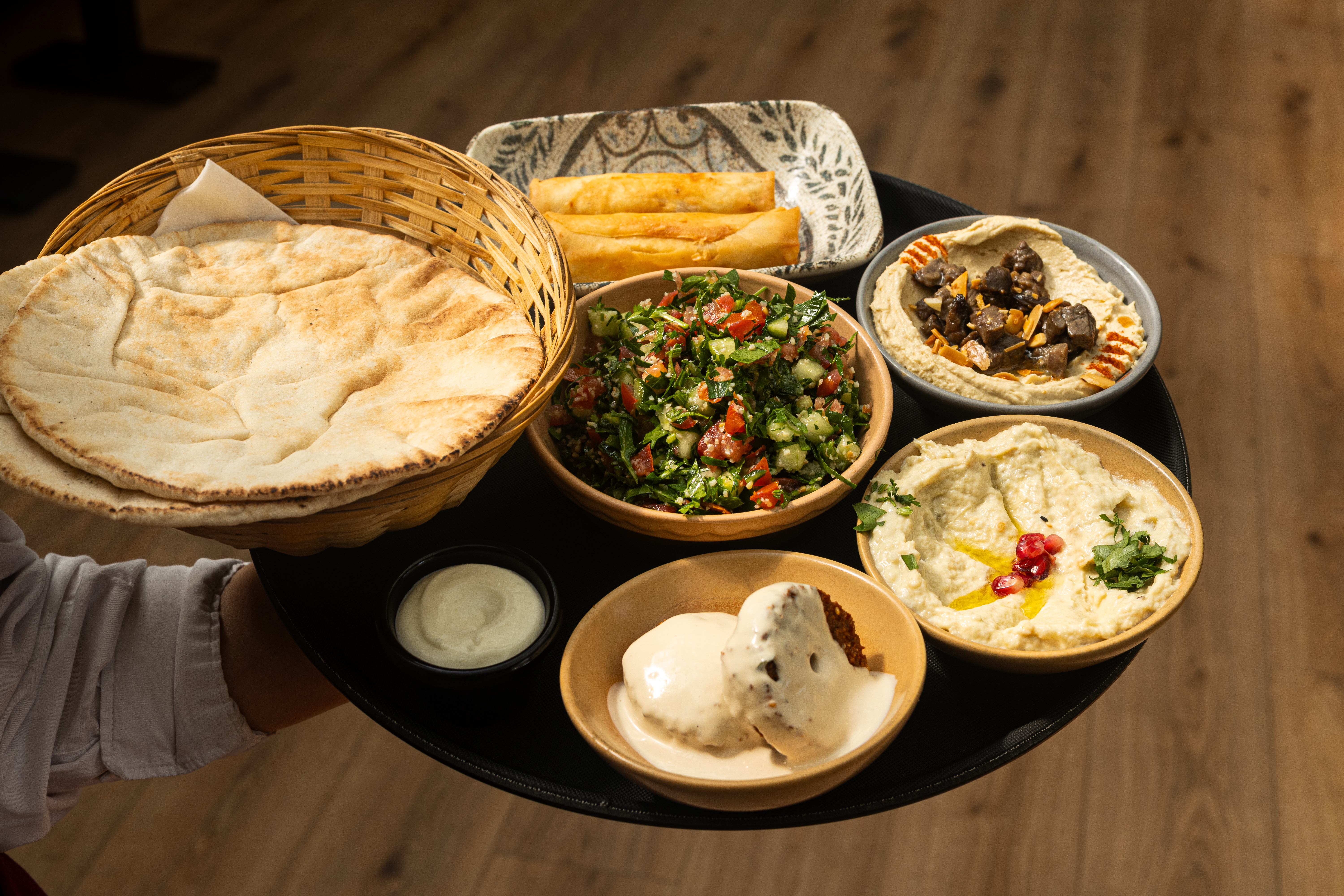 Server carrying a tray of mezze, hummus and flatbread to a table